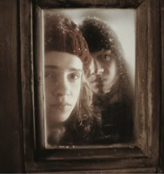 two people are reflected in a mirror on a wooden door, one is wearing a red beanie and the other is looking at her