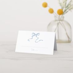 a card with a bow on it sitting next to a vase filled with yellow flowers