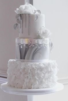 a three tiered wedding cake with white flowers on the top and silver decorations on the bottom