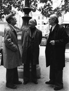 black and white photograph of three men standing in front of a fountain talking to each other