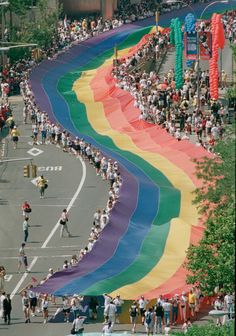 a large rainbow flag is being carried down the street