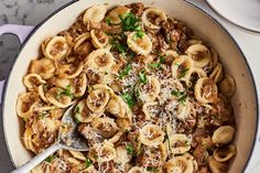 a skillet filled with pasta and meat on top of a table next to two plates