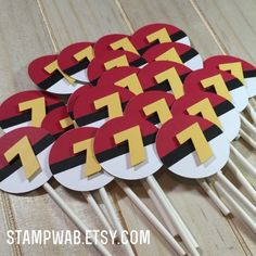 a bunch of red and black cupcake toppers with yellow arrows on them sitting on a wooden table