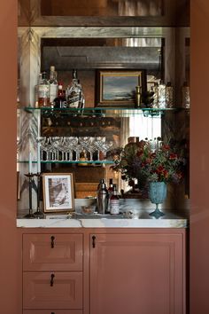 a kitchen counter topped with lots of bottles and glassware next to a shelf filled with glasses