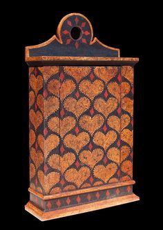 an ornate wooden box with red and gold designs on the front, sitting against a black background