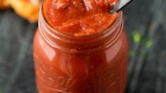 a jar filled with tomato sauce and a spoon in the jar next to some bread