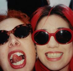 two women with red hair and sunglasses are posing for the camera, one is sticking her tongue out