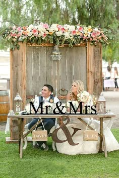 a man and woman sitting at a table in front of a sign that says mr and mrs