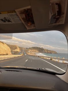 the view from inside a vehicle looking out at an ocean and beach with cliffs in the distance