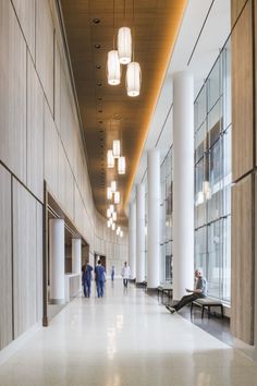 people are walking through the lobby of an office building with large columns and floor to ceiling windows