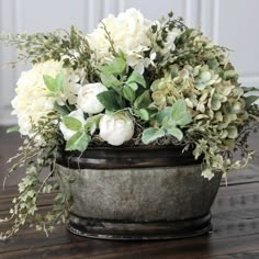 a flower pot with white flowers and greenery in it sitting on a wooden table