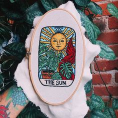 the sun is depicted in this embroidery pattern on a white piece of cloth next to some green plants