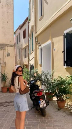 a woman standing next to a motor scooter on a brick road in front of buildings