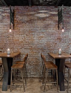 a brick wall with several tables and chairs in front of it that have candles on them