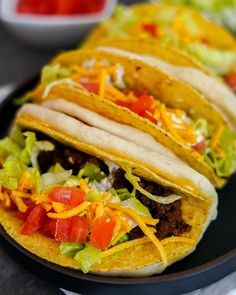 three tacos on a plate with lettuce, tomato and cheese in the middle