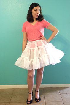 a woman standing in front of a wall wearing a pink shirt and white tulle skirt