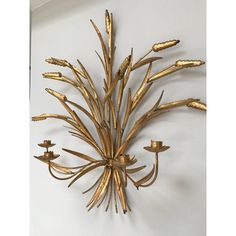 a gold metal wall sculpture with flowers on it's sides and leaves in the middle