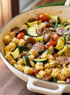 a skillet filled with pasta, sausage and zucchini salad on top of a wooden table