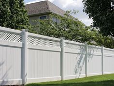 a white vinyl fence in front of a house with trees and grass on the side