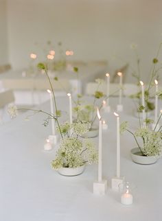 there are many white candles and flowers in the vases on the table with each other