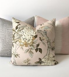 three pillows with flowers on them sitting next to each other in front of a white wall