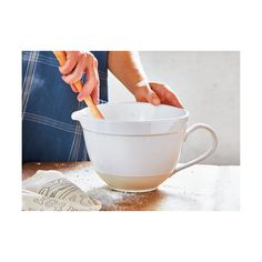 a person holding a carrot in a white bowl on top of a wooden table next to a paper towel