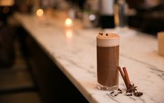 a drink sitting on top of a counter next to cinnamons and anisette