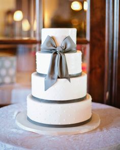 a three tiered white wedding cake with grey ribbon and bow on the top layer