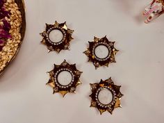 four pieces of jewelry sitting on top of a white table next to a bowl of nuts