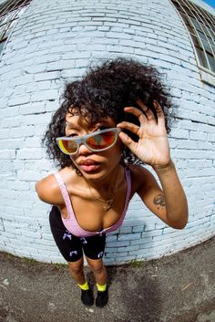 a woman wearing sunglasses is posing in front of a white brick wall with her hands on her head