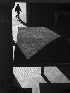 black and white photograph of a person walking down the street with their shadow on the ground