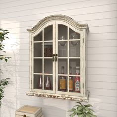 an old china cabinet with glass doors on the side of a white house next to a potted plant