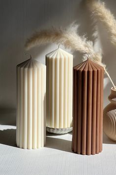 three candles sitting next to each other in front of a vase and some dried grass