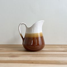 a brown and white pitcher sitting on top of a wooden table