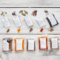 various spices and herbs laid out on a white wooden table with labels for different types of seasonings