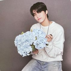 a young man holding a bunch of blue flowers