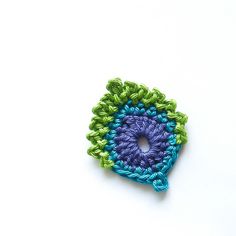 a crocheted square with a blue and green center on a white table top