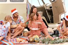 a group of people sitting on top of a beach next to a van and food