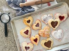 heart shaped pastries on a baking sheet with a cookie scooper next to them