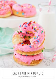 three donuts with pink frosting and sprinkles next to a glass of milk