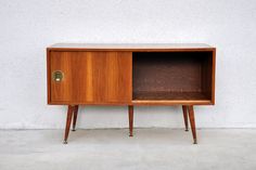 an old wooden cabinet with brass handles on the door and drawer is standing against a white wall