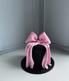 a black hat with a pink bow on the top and bottom, sitting in front of a white wall