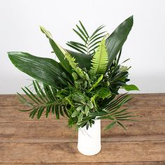 a plant in a white vase sitting on a wooden table next to a wood plank