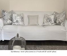 a white couch with lots of pillows on it and a bird cage in the corner