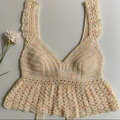 a crocheted top is shown with a flower on the table next to it