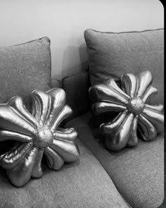 two silver pillows sitting on top of a couch next to each other in front of a white wall