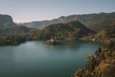 an island in the middle of a lake surrounded by trees and mountains with a church on it