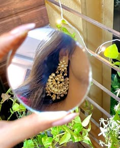 a woman holding up a mirror with some plants in it