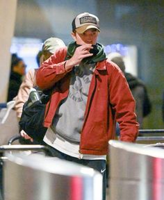 a man in a red jacket and hat is looking at his cell phone while walking through an airport