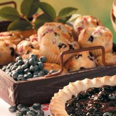 blueberry muffins in a wooden tray next to a pie on a table